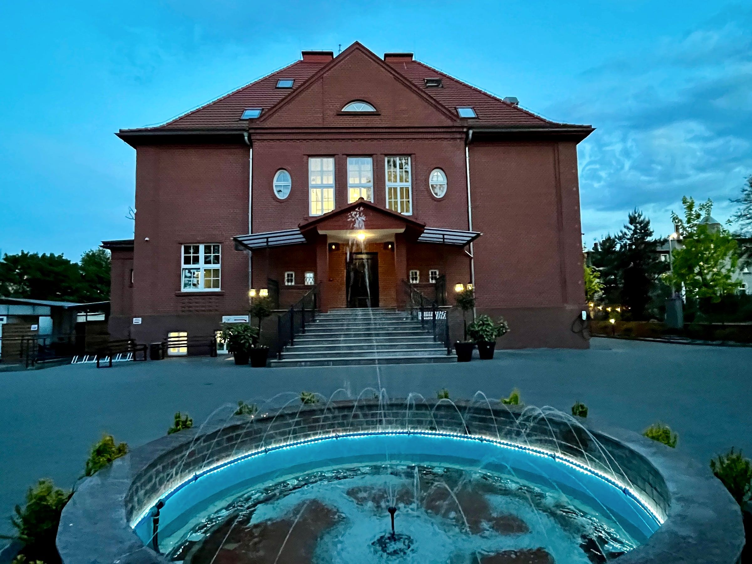 Ceglany budynek z oświetlonym wejściem i fontanną o zmierzchu
