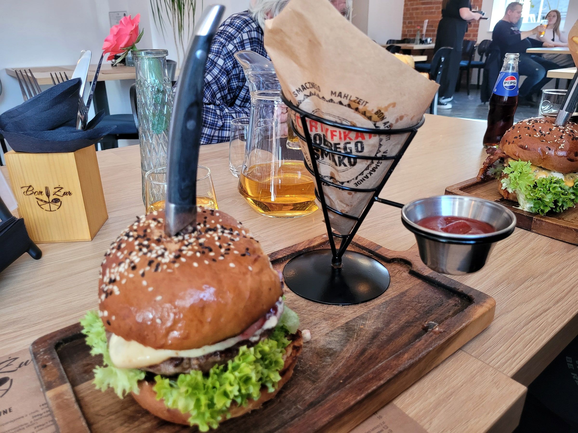 Burger kraftowy z serem i sałatą na drewnianej desce, obok frytki w papierowym rożku