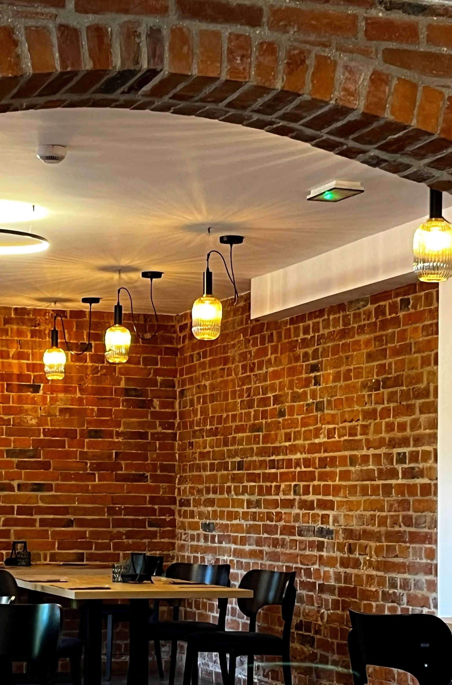 Sala restauracji Bon Żur: ceglany łuk sklepienia, ceglane ściany i bursztynowe lampy nad stolikami