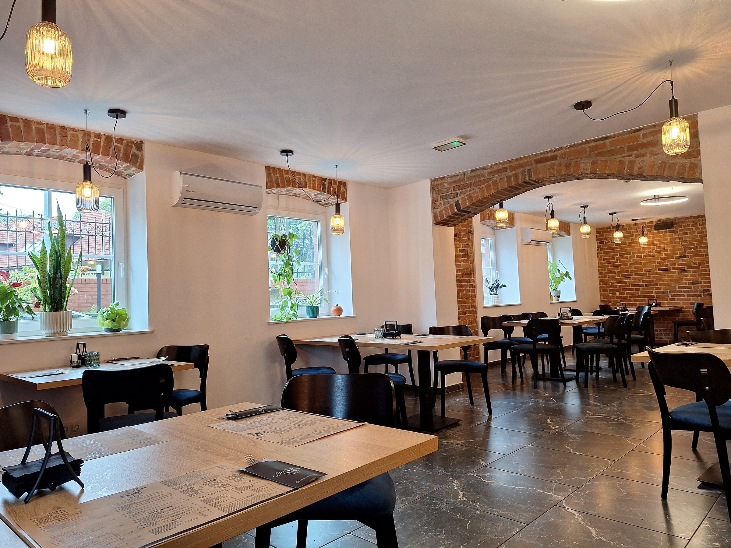 Sala restauracji Bon Żur z ceglanymi łukami, stołami i lampami, gotowa na przyjęcie